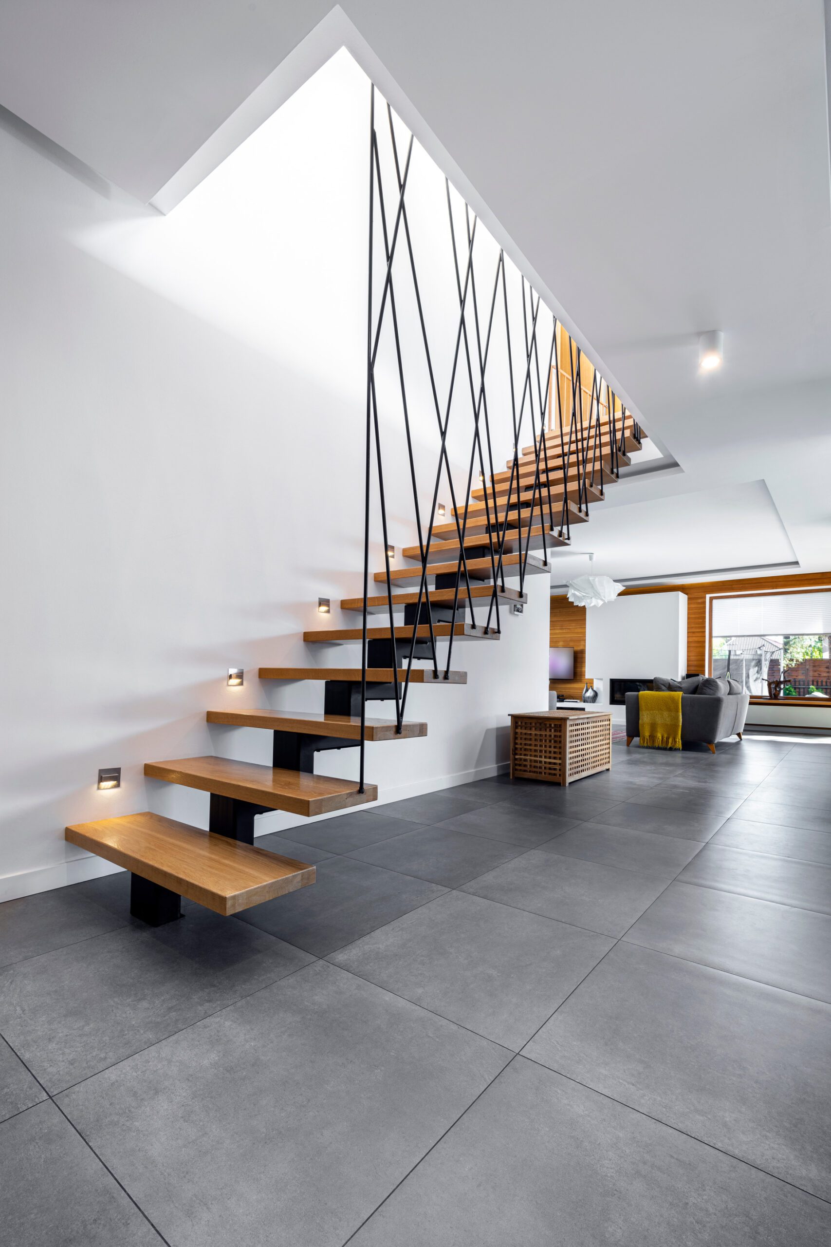 A mid-century modern living room with designer furniture, an indoor garden with a fountain, large windows revealing a forest landscape at sunset, and a potted tree, creating a serene and inviting atmosphere.