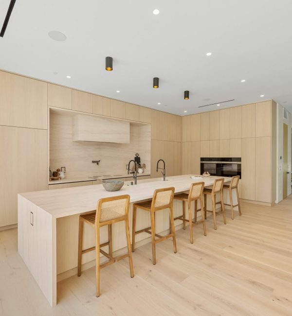 Modern kitchen interior with light wood cabinetry and island. A mid-century modern living room with designer furniture, an indoor garden with a fountain, and a large window revealing a forest landscape at sunset.