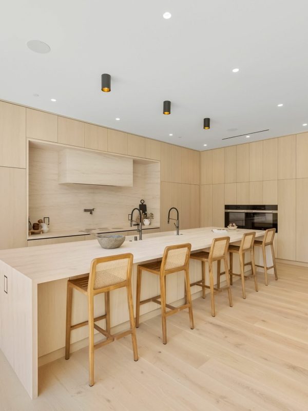 Modern kitchen interior with light wood cabinetry and island. A mid-century modern living room with designer furniture, an indoor garden with a fountain, and a large window revealing a forest landscape at sunset.